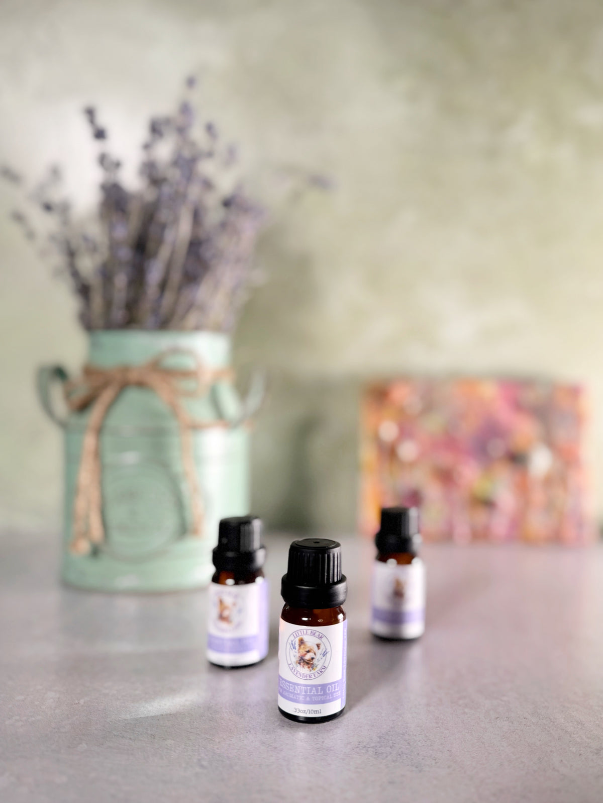 Three 10 ml bottles of steam-distilled lavender essential oil beside a vase of lavender